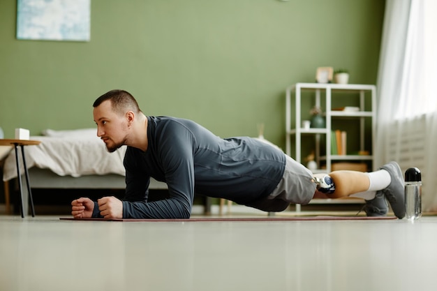 Seitenansicht Porträt eines Mannes mit Beinprothese, der zu Hause trainiert und Plankenübungen im Spa macht