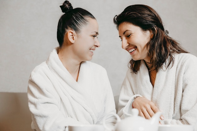 Seitenansicht Porträt von zwei reizenden jungen kaukasischen Frau, die Spaß lachend sitzt in einer Wellness-Spa-Massage gekleidet in Bademänteln nach Prozeduren.