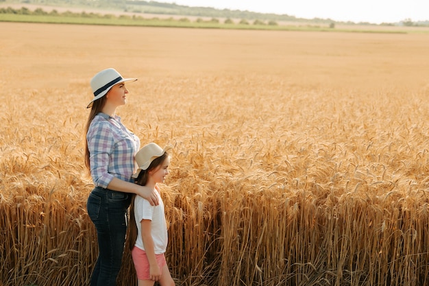 Seitenansicht Porträtfamilie Bauernmutter mit Tochter in Hüten im Weizengoldfeld Agro-Spaziergang in...