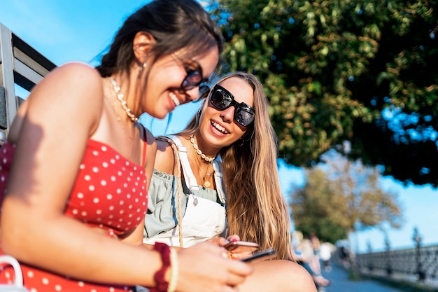 Seitenansicht von attraktiven jungen Freundinnen, die im Sommer auf der Stadtstraße telefonieren