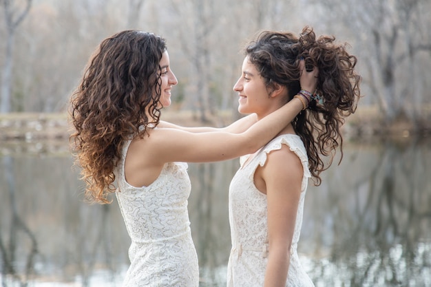 Seitenansicht von den netten Zwillingsschwestern, die miteinander Haar lächeln und kämmen