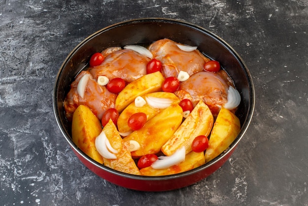 Seitenansicht von rohem Hühnerfleisch mit Kartoffelgemüse im Topf auf grauem Hintergrund