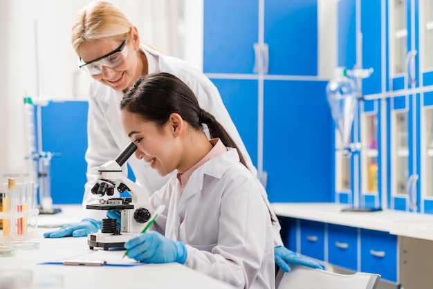 Foto seitenansicht von wissenschaftlerinnen, die am mikroskop im labor arbeiten