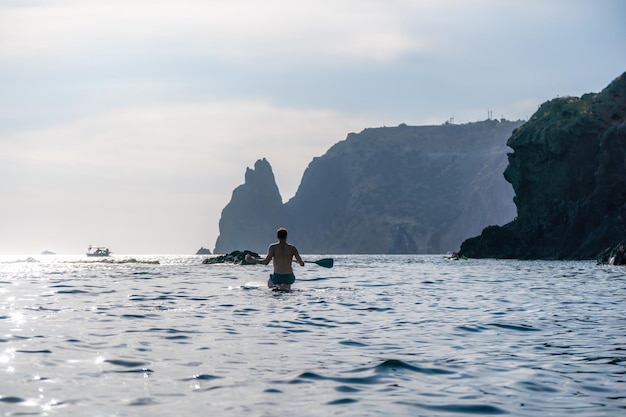 Seitenansichtfoto eines Mannes, der auf dem SUP-Board schwimmt und entspannt Sportlicher Mann im Meer auf dem Stand Up Paddle Board SUP Das Konzept eines aktiven und gesunden Lebens im Einklang mit der Natur