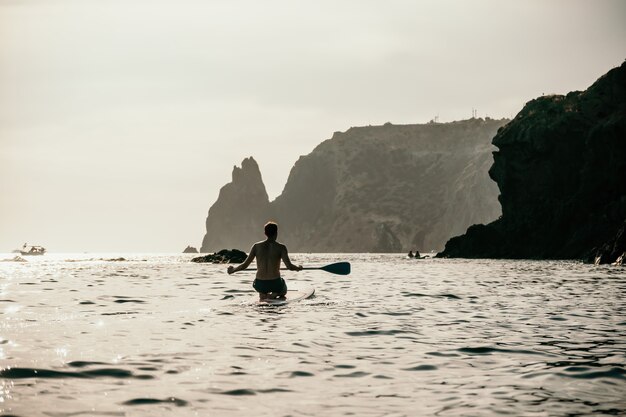 Seitenansichtfoto eines Mannes, der auf dem SUP-Board schwimmt und sich entspannt sportlicher Mann im Meer auf dem Stand