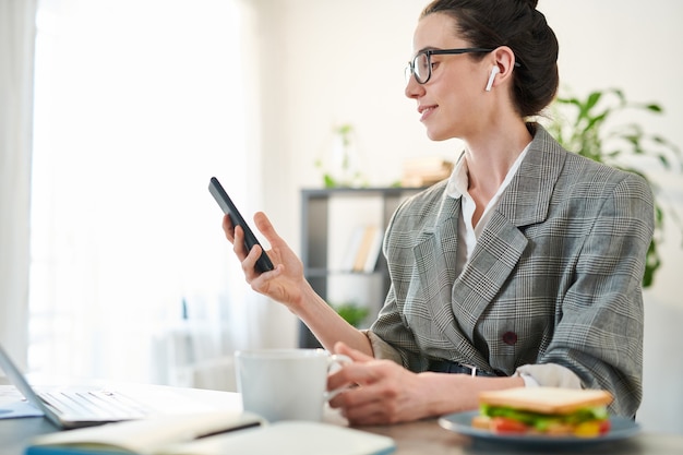 Seitenansichtporträt der jungen Geschäftsfrau, die Smartphone am Arbeitsplatz und lächelnd, Kopienraum verwendet