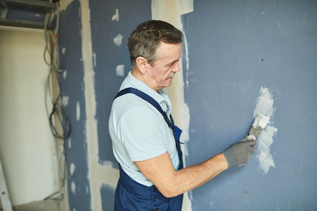 Seitenansichtporträt des älteren Mannes, der an Trockenmauer arbeitet, während Haus renoviert, Raum kopiert