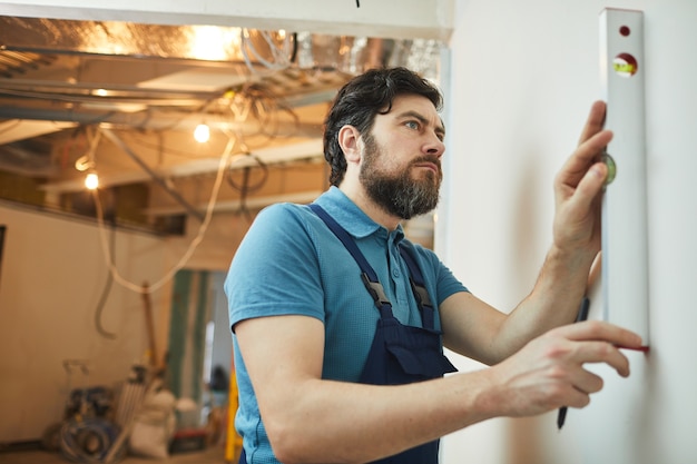 Seitenansichtporträt des bärtigen Bauarbeiters, der das Niveau der Wand beim Renovieren des Hauses misst, Raum kopieren