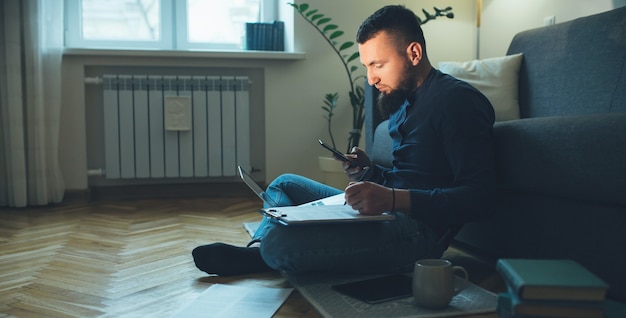 Seitenansichtporträt des kaukasischen Mannes mit Bart, der mit jemandem den Boden unter Verwendung eines Laptops beim Arbeiten mit einigen Dokumenten plaudert