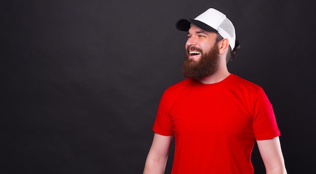 Seitenansichtporträt des verblüfften lächelnden bärtigen Hipster-Mannes, der weiße Kappe trägt