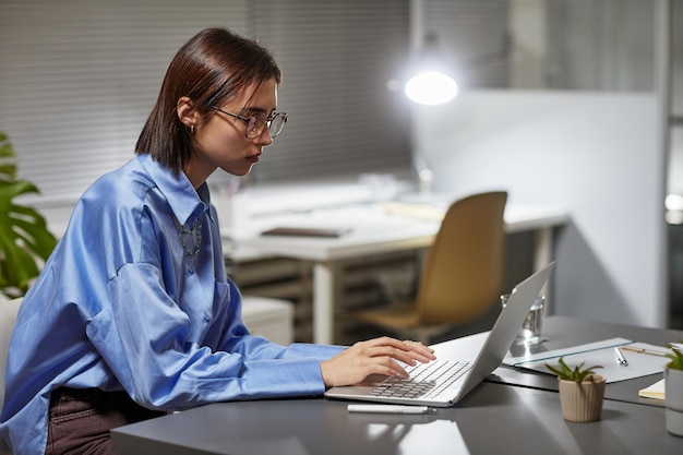 Seitenansichtporträt einer jungen Frau, die Laptop im Büro verwendet, während sie spät in der Nacht Kopierraum arbeitet