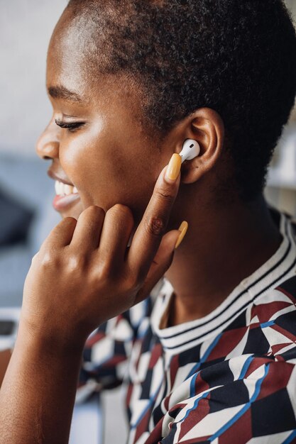 Seitenansichtporträt einer lächelnden afrikanischen Frau, die Musik in Airpods-Nahaufnahmeporträt hört