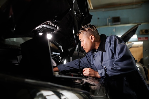 Seitenansichtporträt einer Mechanikerin, die einen LKW-Motor in einer Garage mit Akzentlicht repariert