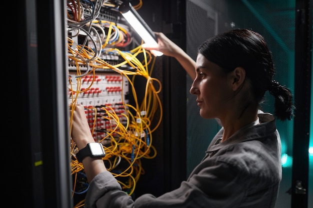 Seitenansichtporträt einer Netzwerkingenieurin, die Kabel im Serverschrank anschließt, während sie mit einem Supercomputer im Rechenzentrum arbeitet