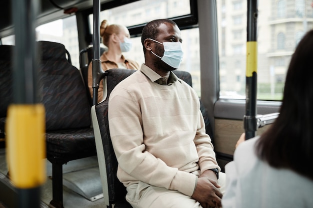 Seitenansichtporträt eines afroamerikanischen Mannes, der eine Maske im Bus trägt, während er mit öffentlichen Verkehrsmitteln in der Stadt unterwegs ist, Kopierraum