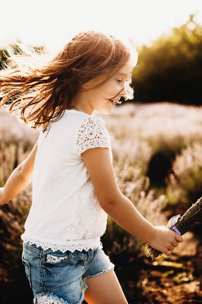 Seitenansichtporträt eines glücklichen Kindes, das in einem Bio-Blumenfeld gegen Sonnenuntergangslachen spielt.