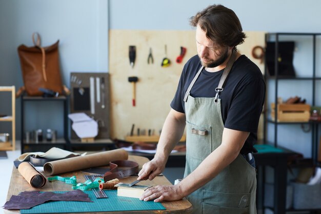 Seitenansichtporträt eines männlichen Handwerkers, der mit Leder in Werkstattstudio-Kleinunternehmenskonzept-Co ...