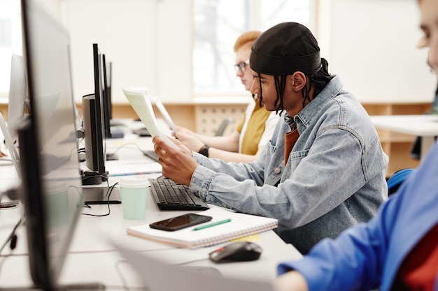 Seitenansichtporträt eines schwarzen jungen Mannes, der Computer in der College-Bibliothek benutzt, während er für Exa recherchiert