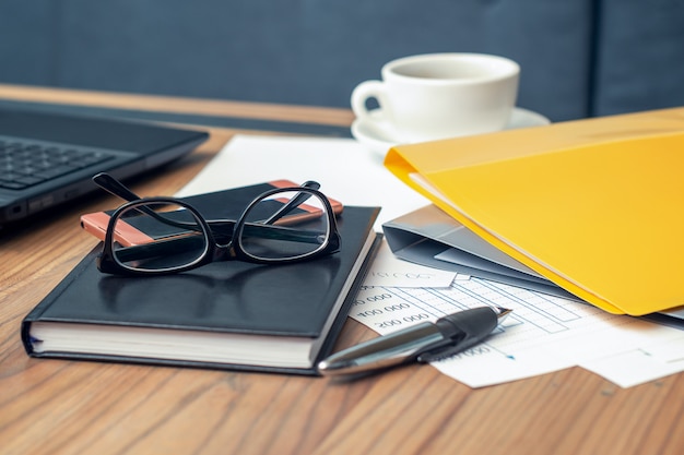 Seitenansichtsbrille, Smartphone, Laptop, Notizbuch und Stift auf dem Holztisch.