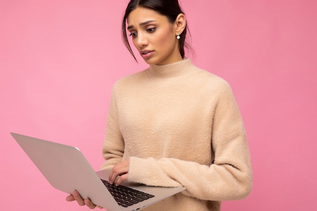 Seitennahes Profilfoto einer charmanten, ziemlich traurigen jungen Dame, die einen Laptop isoliert über dem Wandhintergrund hält und auf das Netbook-Tipptext blickt
