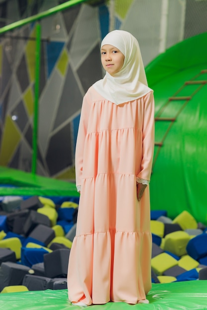 Seitenporträt eines kleinen muslimischen Mädchens, das einen Hijab trägt. Konzept der muslimischen Kleidung für Kinder. vor dem Hintergrund des Spielplatzes.