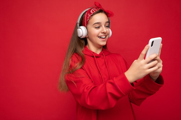 Seitenprofilfoto des lächelnden positiven attraktiven brünetten mädchens mit rotem hoodie isoliert auf rot