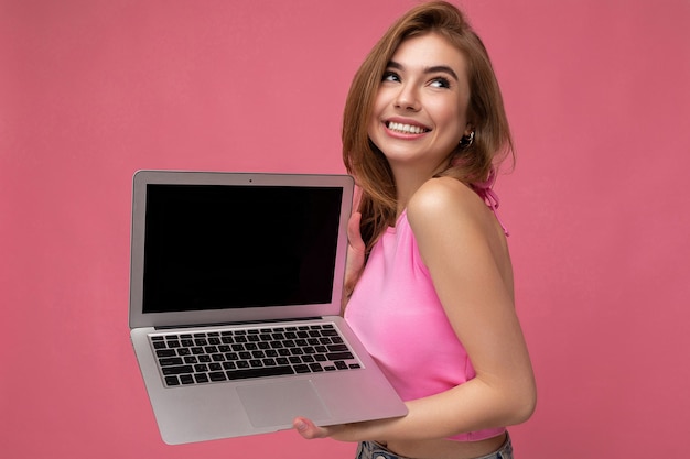Seitenprofilfoto einer glücklich lächelnden schönen jungen blonden Frau, die einen Computer-Laptop in Rosa hält