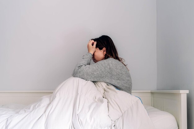 Seitliche Ansicht einer Frau, die zu Hause auf dem Bett sitzt