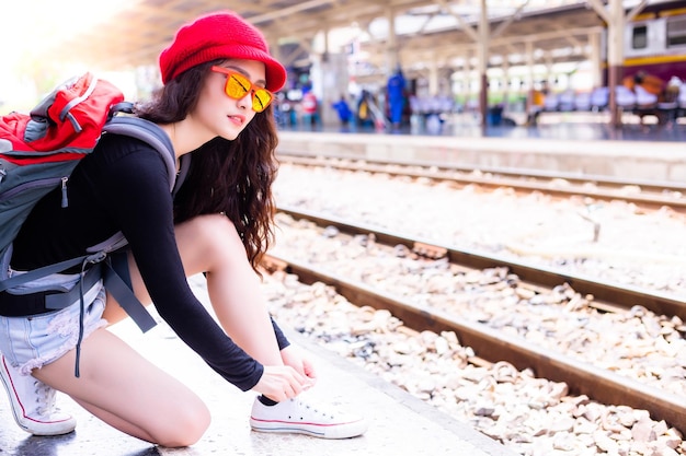 Foto seitliche ansicht einer jungen frau mit rucksack, die schnürsenkel am bahnhofsplatform bindet