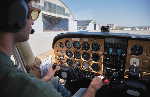 Seitliche Ansicht von einem jungen männlichen Flieger in lässiger Kleidung und Kopfbedeckung, der während des Betriebs eines modernen Vier-Sitz-Flugzeugs Knöpfe auf dem Armaturenbrett drückt