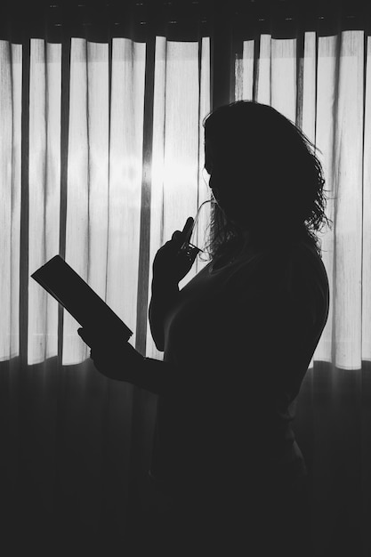 Seitliche Sicht auf die Silhouette einer Frau, die zu Hause ein Buch hält