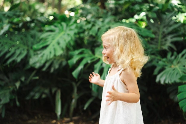 Foto seitliche sicht von süßem kaukasischen hübsches blondes zweijähriges mädchen kleinkind kind unter großen grünen exotischen monster