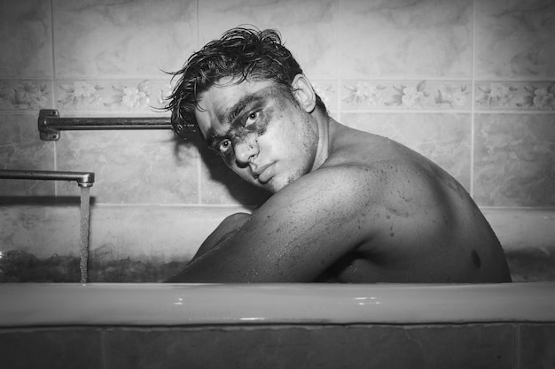 Seitliches Porträt eines hemdlosen Mannes mit Gesichtsfarbe, der in einer Badewanne sitzt
