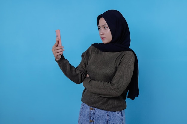 Seja esperto, compre este dispositivo, retrato de uma jovem mulher asiática rindo alto, usando um hijab apontando para o smartphone, mostrando a tela do dispositivo