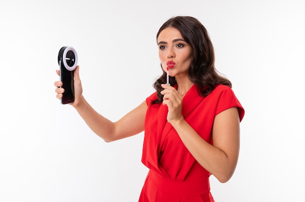 Sekretärin auf dem Hintergrund einer weißen Wand korrigiert Make-up, ein Mädchen schaut in ein Smartphone und malt ihre Lippen