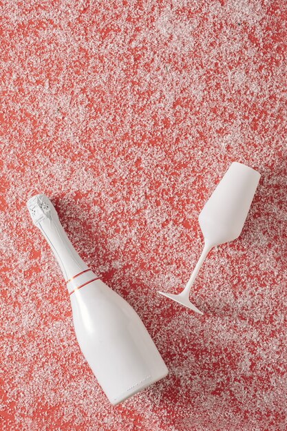 Sektflasche und Glas auf rotem Grund mit weißem Schnee. Minimales Konzept von Weihnachten und Valentinstag oder Jubiläumsfeier