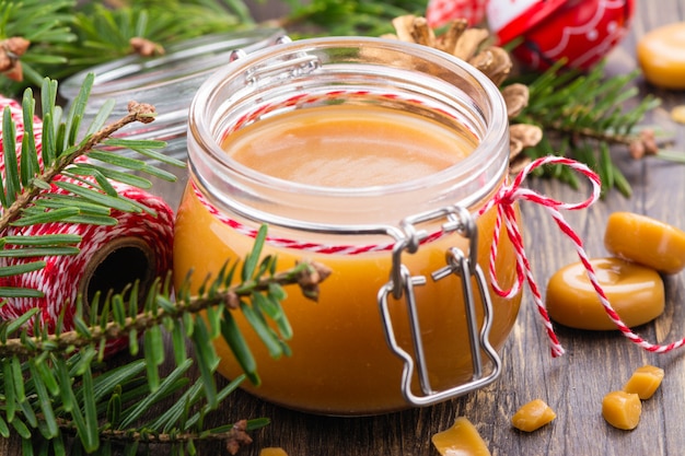 Selbst gemachte gesalzene Karamellsoße in einem Glasgefäß und in einem Weihnachtsdekor auf Holz