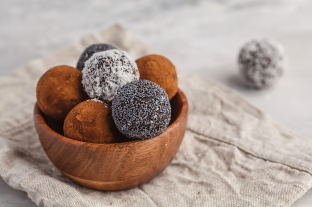 Selbst gemachte gesunde rohe Energie-Bälle des strengen Vegetariers mit Johannisbrotbaum, Mohnblume und Kokosnuss in der hölzernen Schüssel. Gesundes veganes Lebensmittelkonzept.