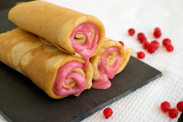 Selbst gemachte Pfannkuchen verdrehten sich mit Beerenmarmelade auf einem Steinbrett.