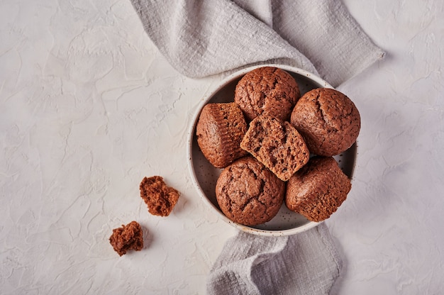 Selbst gemachte Schokoladencupcakes in der Schüssel mit Serviette auf hölzernem hellem Hintergrund Draufsicht kopieren Raum