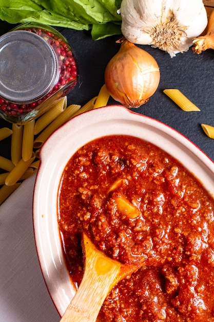 Selbst gemachte Soße des langsamen Kochers Bolognese im roten keramischen Topf und im rohen penne