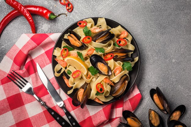 Selbst gemachte Teigwaren-Spaghettis mit Miesmuscheln, Paprikas und Petersilie auf Steinhintergrund.