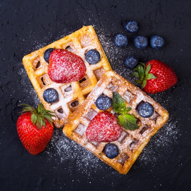 Selbst gemachte traditionelle belgische waffeln mit frischem obst, beeren und zuckerpulver auf schwarzblech.