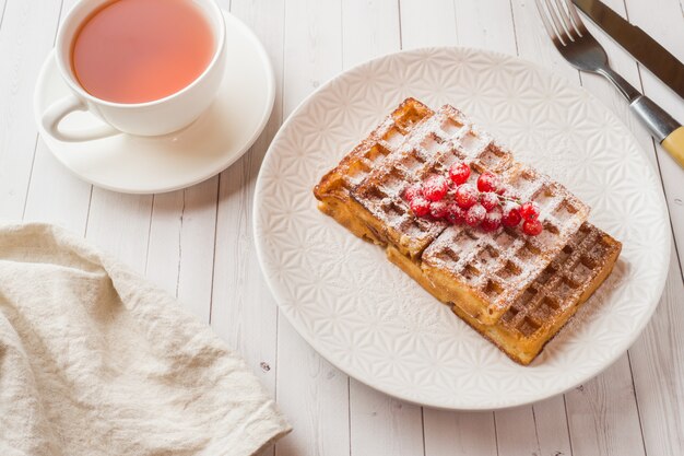 Selbst gemachte Waffeln mit Sommerbeeren auf einer Platte. Eine Tasse Tee auf einem Leuchtpult. Tiefenschärfe