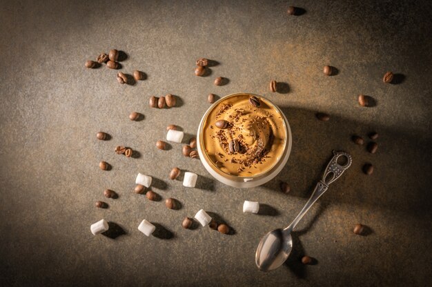 Selbst gemachter Dalalgona-Kaffee auf dunklem Hintergrund. Neben Kaffeebohnen und Marshmallows.