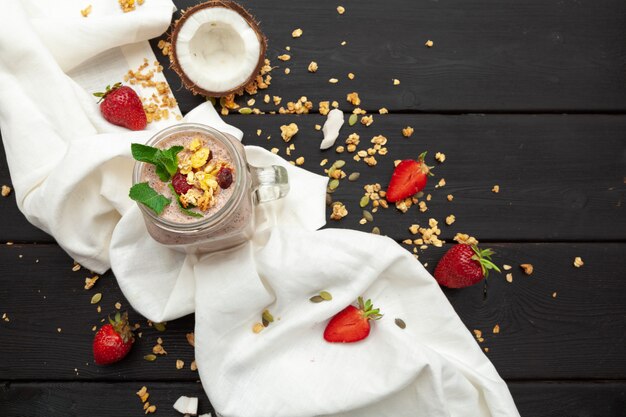 Selbst gemachter Jogurt mit Granola, Frucht und Kokosnuss auf hölzernem Hintergrund