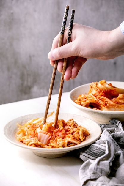 Selbst gemachter koreanischer traditioneller fermentierter Vorspeisen-Kimchi-Kohl, der in der Keramikplatte serviert wird. Essstäbchen in den Händen des Mannes.