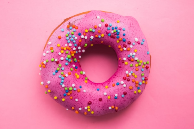 Selbst gemachter Kreiskrapfen mit rosa Zuckerguss und Regenbogenstreuseln