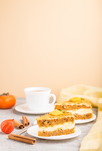 Selbst gemachter Kuchen mit Kaki und Kürbis und einer Tasse Kaffee auf grauer und orange Wand. Seitenansicht, Kopierraum, selektiver Fokus.