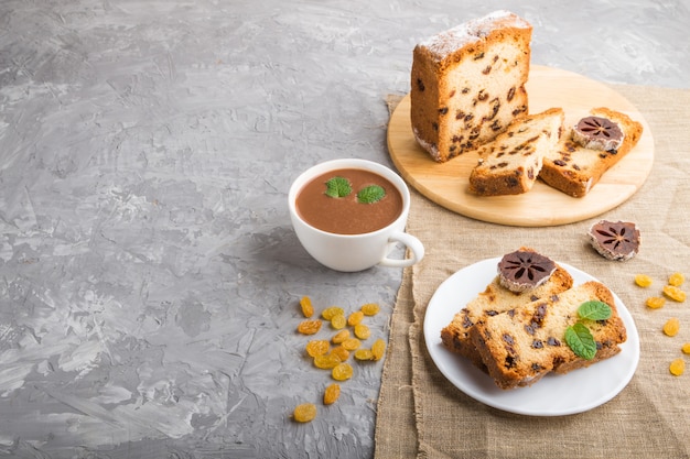 Selbst gemachter Kuchen mit Rosinen, getrockneter Persimone und einer Tasse heißer Schokolade auf einem grauen Betonhintergrund. Seitenansicht, Kopierraum.